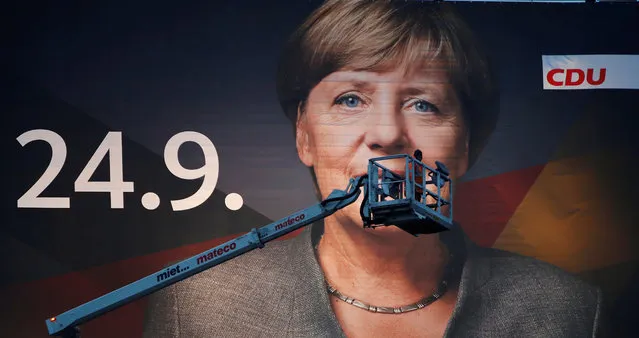 A crane operator steers his mobile crane next to a 18-metre wide “Mega Poster” of Angela Merkel, German Chancellor and leader of the Christian Democratic Union party CDU, after fixing the lights for Merkel's campaign picture for the September 24 general elections, in Duisburg, Germany, September 14, 2017. (Photo by Wolfgang Rattay/Reuters)