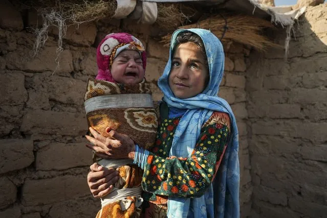 Qandi Gul holds her brother outside their home housing those displaced by war and drought near Herat, Afghanistan. December 16, 2021. Gul’s father sold her into marriage without telling his wife, taking a down-payment so he could feed his family of five children. Without that money, he told her, they would all starve. He had to sacrifice one to save the rest. (Photo by Mstyslav Chernov/AP Photo)