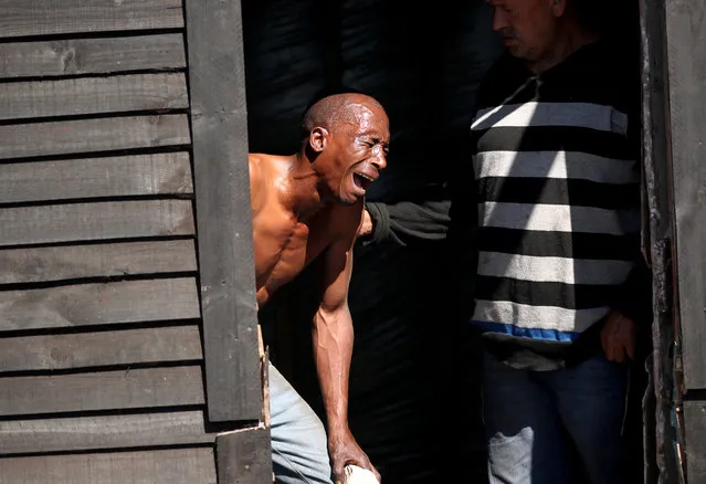 A man weeps and is comforted by a friend as law enforcement officials move in to demolish his shack after Khayelitsha township residents attempted to occupy vacant land during a nationwide lockdown aimed at limiting the spread of the coronavirus disease (COVID-19) in Cape Town, South Africa, April 22, 2020. (Photo by Mike Hutchings/Reuters)
