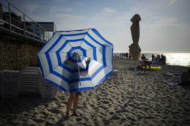 A woman folds a beach umbrella during sunset at the seashore at the Curonian Spit, a 98 kilometers long thin curved sand-dune spit that separates the Curonian Lagoon from the Baltic Sea coast near Lesnoy village, 50 km (32,5 miles) north of Kaliningrad, the westernmost federal subject of Russia, Sunday, August 28, 2022. Hot weather continues in the Kaliningrad region with temperatures and comes up to 30 degrees Celsius (86 Fahrenheit). (Photo by Alexander Zemlianichenko/AP Photo)