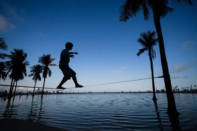 A man walks on a slackline between two palm trees on Copacabana beach in Rio de Janeiro, on 30 July 2016. The city is making last minute preparations for the events and celebrations as the 2016 Rio Olympic Games are set to begin in Rio on August 5 and run until August 21, 2016. (Photo by Leon Neal/AFP Photo)