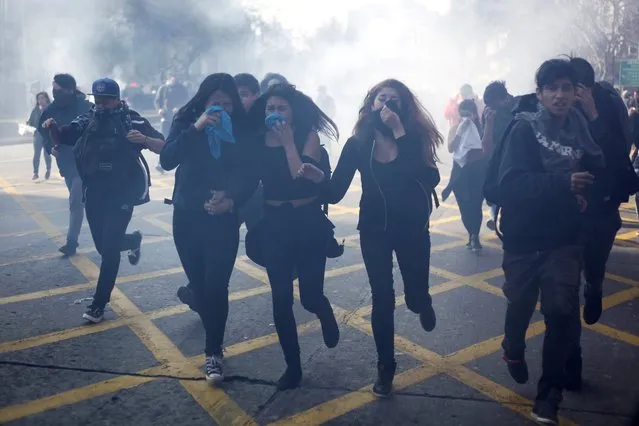 Thousands of students marching to protest a proposed education overhaul promoted by President Michelle Bachelet's administration cover their faces from tear gas, in Santiago de Chile, Chile, 04 August 2016. Chilean students took to the streets once again in the capital and other cities to denounce a proposed higher education overhaul that they say does not go far enough to correct injustices. President Michelle Bachelet pledged during her successful election campaign in 2013 that she would make college free and said the initial phase would aid 70 percent of the poorest students. But a sluggish economy led the government to retreat from that target and the implementation of the plan has been rocky. (Photo by Sebastian Silva/EPA)