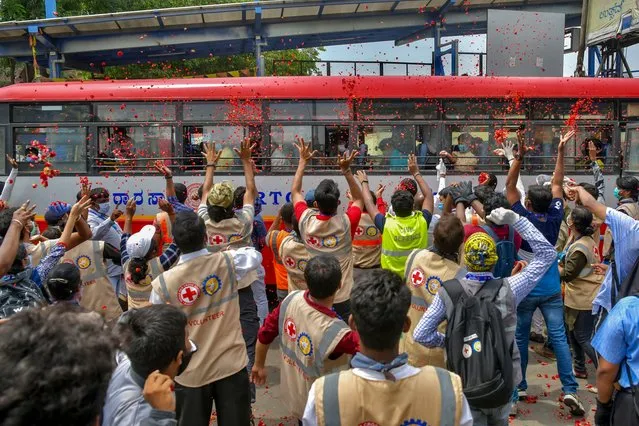 Volunteers of Indian Red Cross and other NGOs shower flower petals on a bus transporting migrant workers and families to their hometowns at a bus stand after the government eased a nationwide lockdown imposed as a preventive measure against the COVID-19 coronavirus, in Bangalore on May 7, 2020. (Photo by Manjunath Kiran/AFP Photo)