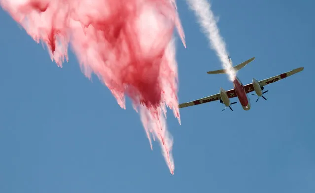 A plane drops retardant over a wildfire near the Cajon Pass in California, Tuesday, August 16, 2016. The fire forced the shutdown of a section of Interstate 15, the main highway between Los Angeles and Las Vegas, leaving commuters stranded for hours. (Photo by James Quigg/The Daily Press via AP Photo)