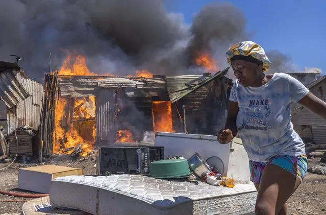 A resident salvages belongings as a fire rages through shacks in Masiphumelele, Cape Town, South Africa, 21 November 2022. Hundreds of residents were displaced with shacks being destroyed by a raging fire in the densely populated Masiphumelele shack district. Masiphumelele is particularly susceptible to fire with poor access routes hampering fire fighting efforts. Fire fighters and residents battle to contain the blaze which the cause is still unknown. (Photo by Nic Bothma/EPA/EFE)