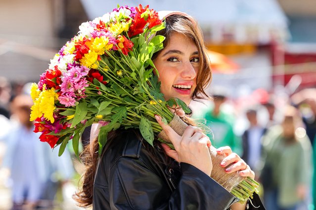 A woman smiles while holding a bouquet of flowers outside the Tajrish Bazaar in central Tehran on March 17, 2025 as people prepare for Nowruz (Noruz), the Persian New Year, which coincides this year with the Muslim holy month of Ramadan. Millions of people across the Middle East, Asia and Eastern Europe celebrate the Nowruz new year festival, which usually falls on March 20, to mark the start of spring. (Photo by Atta Kenare/AFP Photo)