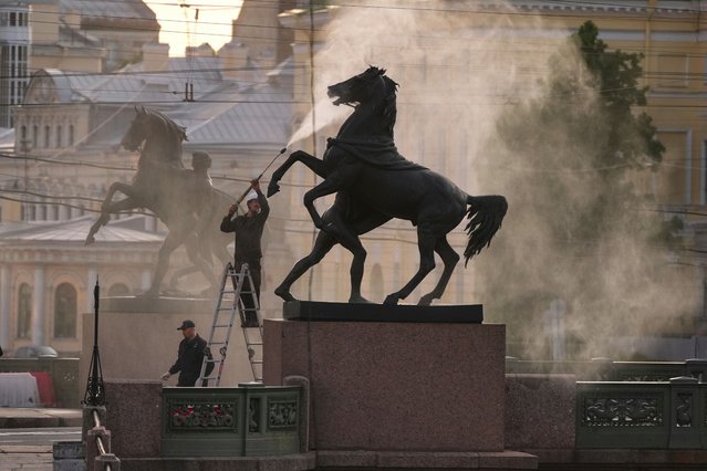 An employee of the Museum of Urban Sculpture cleans one of the four famous horse sculptures of the Anichkov Bridge over the Fontanka River in St. Petersburg, Russia, early Monday, June 2, 2025. (Photo by Dmitri Lovetsky/AP Photo)