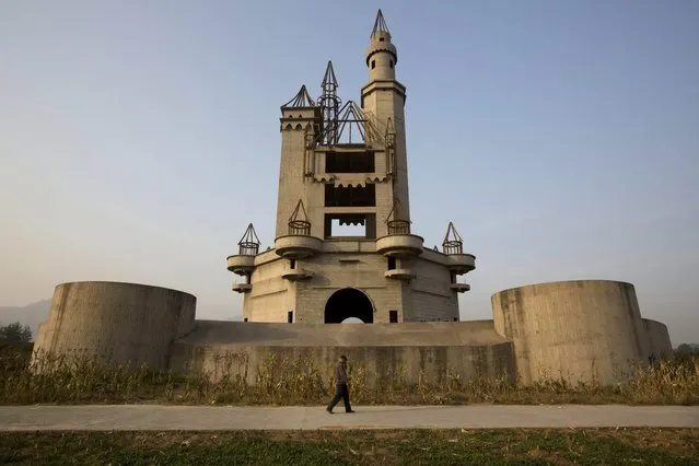 In this October 18, 2014, photo, a man walks past the shell of a castle-like building that was once destined to be part of Asia's biggest amusement park in Beijing, China. Work halted on the project in 1998 due to financial problems and the site has been left as it is until 2013 when developers demolished other parts of the massive park for redevelopment. The castle-like building however remains untouched and a reminder of better times in that part of Beijing's periphery. (Photo by Ng Han Guan/AP Photo)