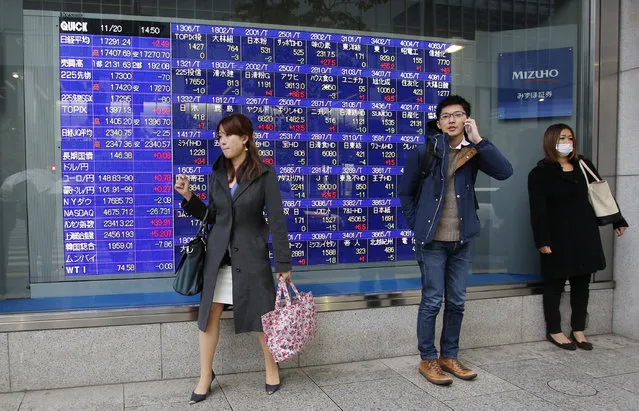 A man uses a mobile phone in front of an electronic stock indicator of a securities firm in Tokyo, Thursday, November 20, 2014. Asian stocks faltered Thursday as China's manufacturing weakened and the latest Fed minutes reminded investors that U.S. interest rates are likely to rise next year. Japan's Nikkei 225 closed at 17,300.86 Thursday. (Photo by Shizuo Kambayashi/AP Photo)