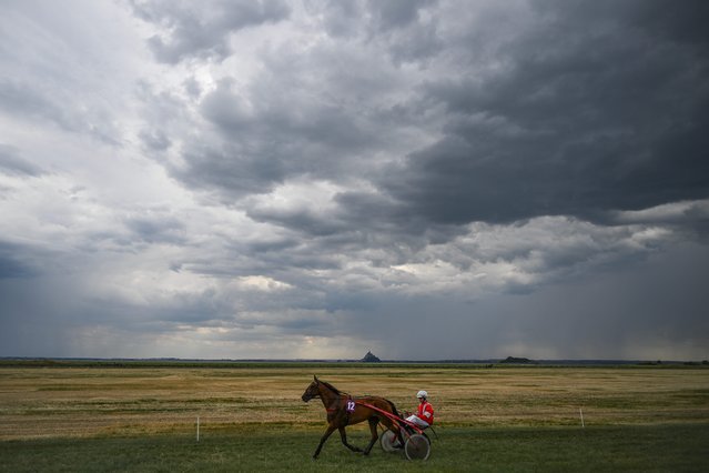 A horse rides on the Genet race course with the Mont-Saint-Michel on the backgroun, to mark its 130th anniversary, in Genet, northwestern France, on July 13, 2025. (Photo by Lou Benoist/AFP Photo)