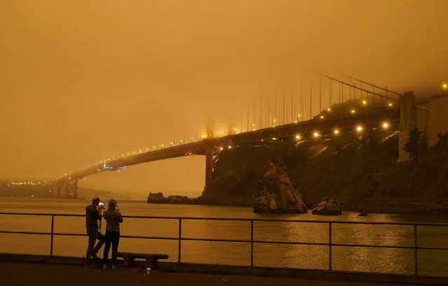 Patrick Kenefick, left, and Dana Williams, both of Mill Valley, Calif., record the darkened Golden Gate Bridge covered with smoke from wildfires Wednesday, September 9, 2020, from a pier at Fort Baker near Sausalito, Calif. The photo was taken at 9:47 a.m. in the morning. (Photo by Eric Risberg/AP Photo)