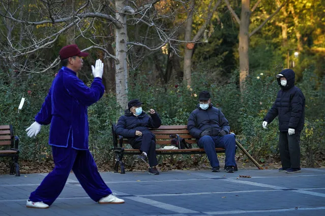People wearing face masks to help curb the spread of the coronavirus chat each other as a man performs morning exercise at a park in Beijing, Monday, November 23, 2020. (Photo by Andy Wong/AP Photo)