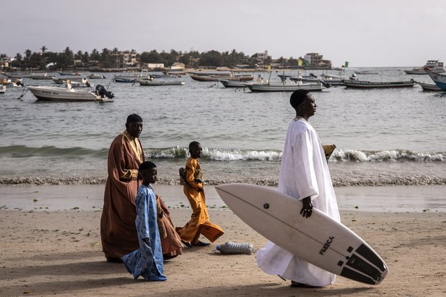 A man dressed in his traditional boubou carries a surf board a he makes his way along Ngor beach to pray during Tabaski (Eid al-Adha) celebrations in Dakar on June 17, 2024. (Photo by John Wessels/AFP Photo)