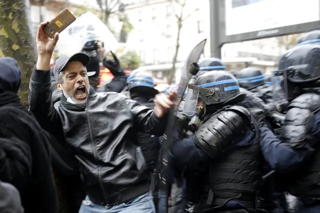 Riot police officers charge a man holding his phone during a protest, Saturday, December 12, 2020 in Paris. Protests are planned in France against a proposed bill that could make it more difficult for witnesses to film police officers. (Photo by Lewis Joly/AP Photo)