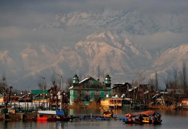 People row their boats in the waters of Dal Lake with the backdrop of snow-covered mountains after a snowfall in Srinagar on December 12, 2020. (Photo by Danish Ismail/Reuters)
