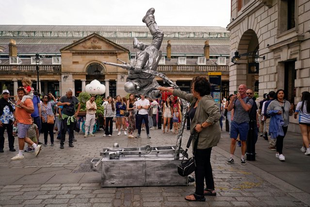 A street performer interacts with a member of the public, outside Covent Garden Market, in London, Saturday, August 3, 2024. (Photo by Alberto Pezzali/AP Photo)