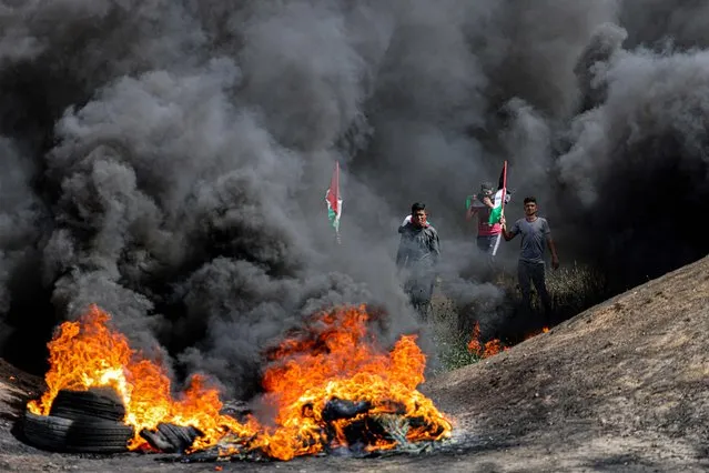 Men with Palestinian flags walk through the fumes from flaming tires during a demonstration along the border with Israel east of Gaza City on April 5, 2023. Israeli police said they had entered to dislodge “agitators” from Jerusalem's al-Aqsa Mosque, a move denounced as an “unprecedented crime” by the Palestinian Islamist movement Hamas. The holy Muslim site is built on top of what Jews call the Temple Mount, Judaism's holiest site. (Photo by Mahmud Hams/AFP Photo)