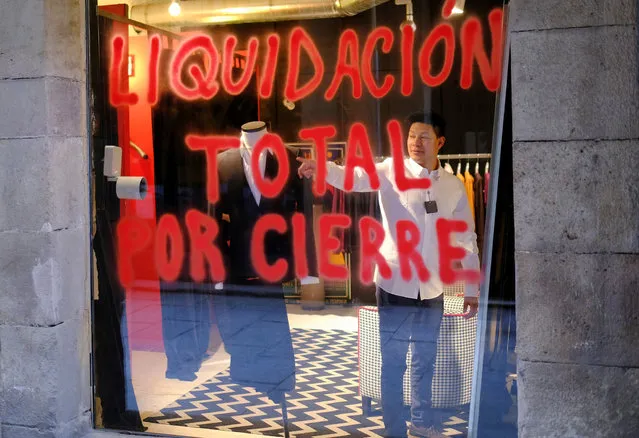 A man tries clothes inside a store with a sprayed window reading “Total sale due to closure” in the neighbourhood of Born, amid the coronavirus disease (COVID-19) pandemic, in Barcelona, Spain on March 11, 2021. (Photo by Nacho Doce/Reuters)