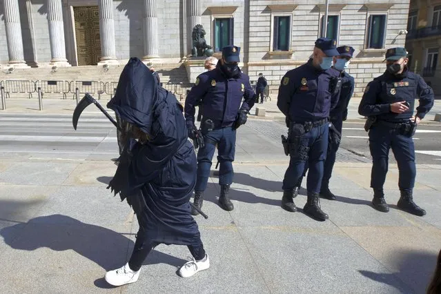 An anti Euthanasia protester walks in front of police officers outside the Spanish Parliament in Madrid, Spain, Thursday, March 18, 2021. Spain has become the seventh country in the world and fourth in Europe to allow physician-assisted suicide and euthanasia for long-suffering patients of incurable diseases or unbearable permanent conditions. The parliament's lower house on Thursday gave the final go-ahead to the euthanasia bill in a 202-140 vote with two abstentions. (Photo by Paul White/AP Photo)