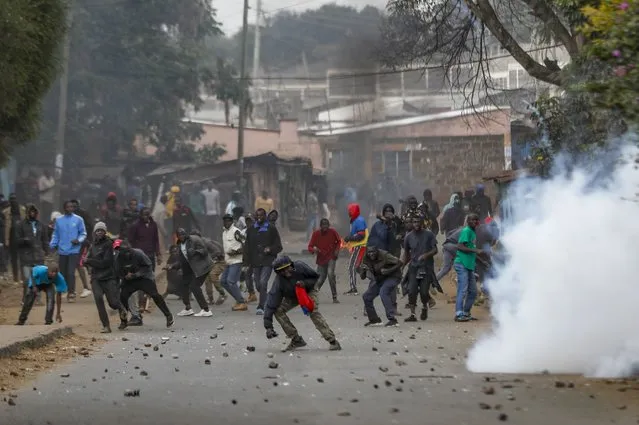 Protesters throw rocks at police during clashes next to a cloud of teargas in the Kibera area of Nairobi, Kenya Wednesday, July 19, 2023. Kenyans were back protesting on the streets of the capital Wednesday against newly imposed taxes and the increased cost of living. (Photo by Brian Inganga/AP Photo)