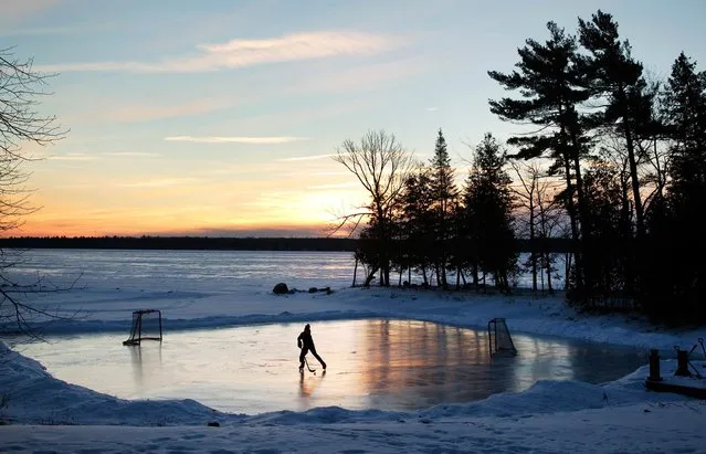 A youth plays pond hockey as the sun rises on Pigeon Lake in the region of Kawartha Lakes Ontario February 4, 2015. (Photo by Fred Thornhill/Reuters)