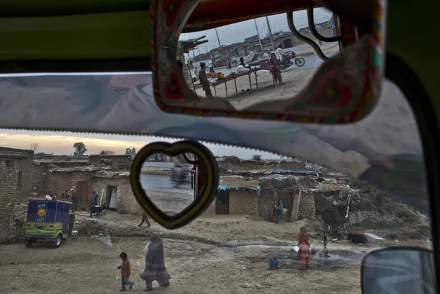 Seen through the windshield and mirrors of a rickshaw parked facing a slum that hosts Afghan refugees and internally displaced Pakistanis from tribal areas, a boy, top, prepares meat on a grill for customers, while a group of men, left, work outside a mud house on the outskirts of Islamabad, Pakistan, Sunday, February 15, 2015. (Photo by Muhammed Muheisen/AP Photo)