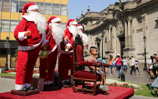 A child poses for a picture with Santa Claus figures, next to the government palace (R), in downtown Lima, Peru, December 11, 2016. (Photo by Mariana Bazo/Reuters)
