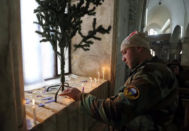 An Iraqi soldier lights candles during Christmas celebrations at the al-Tahira al-Kubra church in the formerly IS held town of al-Hamdaniya, some 13km east of Mosul, Iraq, 25 December 2016. Hundreds of Iraqi Christians held their prayers at a church in the recently recaptured town of Hamdaniya, for the first time since 2014, with the attendance of the US-led coalition officers and senior Iraqi officers. (Photo by Ahmed Jalil/EPA)