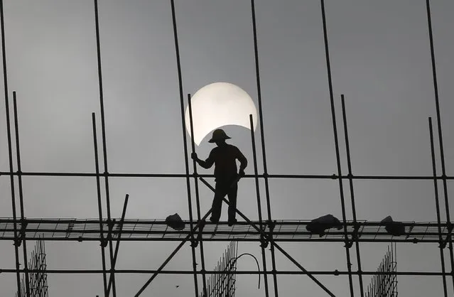 A partial solar eclipse is seen as a labourer works at a construction site in Phnom Penh, Cambodia, March 9, 2016. (Photo by Samrang Pring/Reuters)