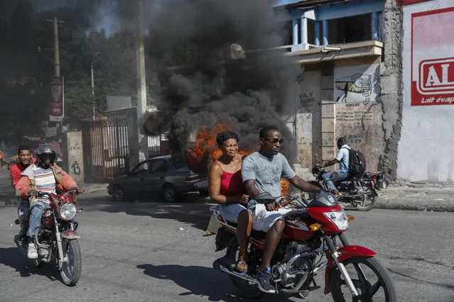 Motorcyclists drive past burning tires set fire to protest gas shortages in Port-au-Prince, Haiti, Thursday, October 21, 2021. (Photo by Joseph Odelyn/AP Photo)