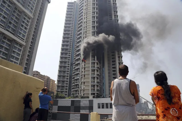 People watch a fire in a 61-story luxury apartment building in Mumbai, India, Friday, October 22, 2021. Television images showed heavy black smoke billowing into the sky from the 19th floor apartment on Curry Road in south Mumbai, India's financial and entertainment capital. Fires are common in India, where building laws and safety norms are often flouted by builders and residents. (Photo by AP Photo/Stringer)
