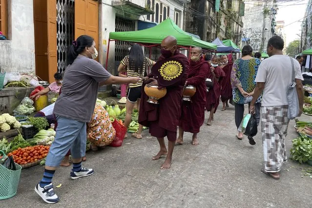 Buddhist monks collect alms from people during their morning walk at the Bogalay Zay Market in Botahtaung township in Yangon, Myanmar on November 12, 2021. (Photo by AP Photo/Stringer)