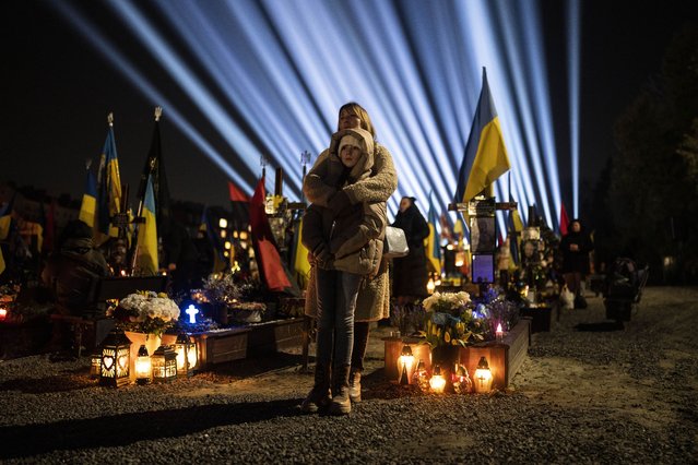A woman and her daughter stand as they listen to a prayer for fallen soldiers at Lviv cemetery, western Ukraine, on Thursday, February 23, 2023. Family members gathered at the military cemetery in Lviv for a “lights of memory” event to honor those who died fighting Russian invasion. (Photo by Petros Giannakouris/AP Photo)