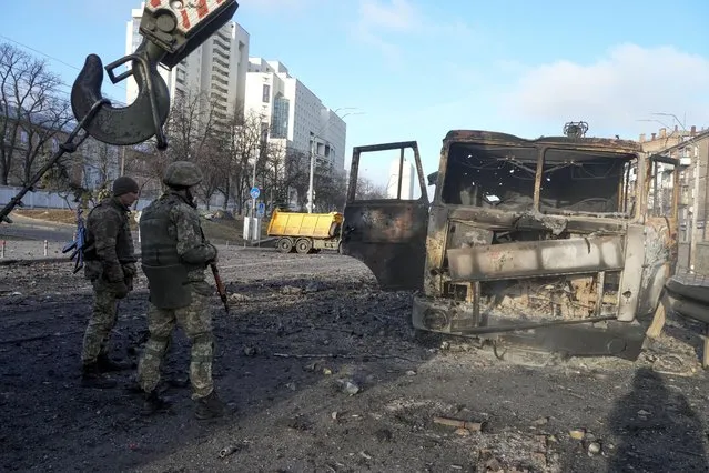 Ukrainian soldiers stand next to a burnt military truck, in a street in Kyiv, Ukraine, Saturday, February 26, 2022. (Photo by Efrem Lukatsky/AP Photo)