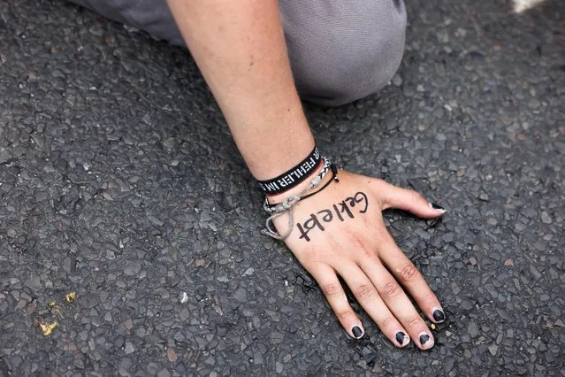 The hand of an Extinction Rebellion activist, with a word reading “glued”, is glued to the road during a protest to demand actions against climate change, near the Brandenburg Gate in Berlin, Germany on August 16, 2021. (Photo by Christian Mang/Reuters)