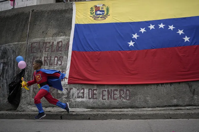 A child dressed as “Super Bigote”, or Super Moustache, runs past a Venezuelan flag in the Catia neighborhood of Caracas, Venezuela, Monday, February 28, 2022. The “Super Bigote” character is a Venezuelan superhero based on Venezuelan President Nicolas Maduro. (Photo by Matias Delacroix/AP Photo)