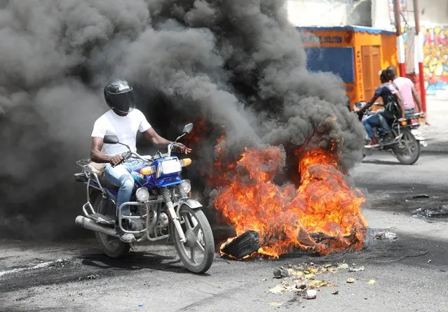 Motorcyclists ride past a burning roadblock during protests demanding that the government of Prime Minister Ariel Henry do more to address gang violence including constant kidnappings, in Port-au-Prince, Haiti on March 29, 2022. (Photo by Ralph Tedy Erol/Reuters)