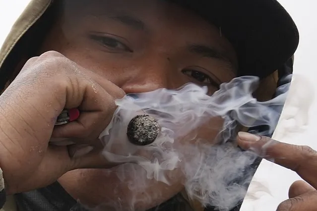 A man smokes a marijuana cigarette as he takes part in a march marking World Cannabis Day, officially observed annually on April 20th, to call for the full legalization of the drug in Quito, Ecuador, Thursday, May 5, 2022. The law in Ecuador allows personal use of cannabis of up to 10 grams and limited cultivation at home, but trafficking and sale of cannabis are illegal. (Photo by Dolores Ochoa/AP Photo)