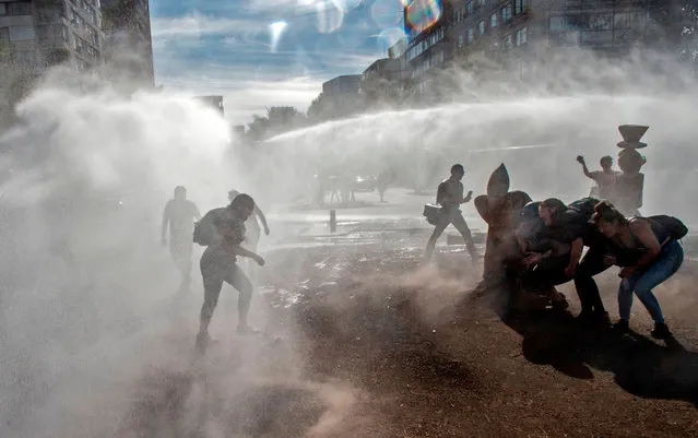 Demonstrators protect themselves from a riot police water cannon spraying over them during clashes with riot police following a protest against Chilean President Sebastian Pinera's government, in Santiago, on December 18, 2019, two months after protests started. Chilean police responded to recent mass protests in a “fundamentally repressive manner”, resulting in serious abuses including unlawful killings and torture, UN investigators said Friday. Chile's crisis erupted over metro fare hikes but quickly escalated into the most severe outbreak of social unrest since the end of the dictatorship of Augusto Pinochet nearly 30 years ago. (Photo by Martin Bernetti/AFP Photo)