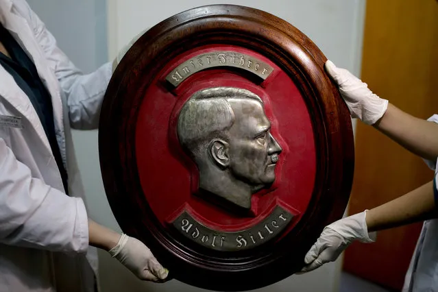 Members of the federal police show a bust relief portrait of Nazi leader Adolf Hitler at the Interpol headquarters in Buenos Aires, Argentina, Friday, June 16, 2017. In a hidden room in a house near Argentina's capital, police believe they have found the biggest collection of Nazi artifacts in the country's history, including a bust relief of Adolf Hitler, magnifying glasses inside elegant boxes with swastikas and even a macabre medical device used to measure head size. Some 75 objects were found in a collector's home in Beccar, a suburb north of Buenos Aires, and authorities say they suspect they are originals that belonged to high-ranking Nazis in Germany during World War II. (Photo by Natacha Pisarenko/AP Photo)