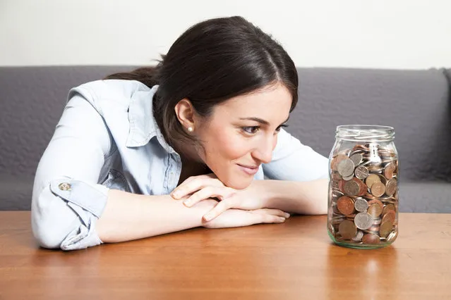 Young woman looking at jar full of coins. (Photo by JamieB/Getty Images)
