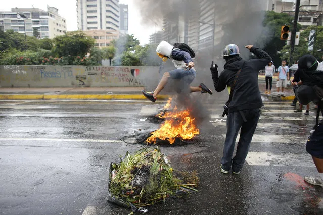 A masked protester jumps over a burning barricade in Caracas, Venezuela, Wednesday, June 28, 2017. The last 24 hours in Venezuela have been volatile, beginning with widespread looting in the coastal city of Maracay on Monday night and continued Tuesday with a police helicopter firing on Venezuela's Supreme Court and Interior Ministry while opposition lawmakers scuffled with security forces assigned to protect the National Assembly. (Photo by Ariana Cubillos/AP Photo)