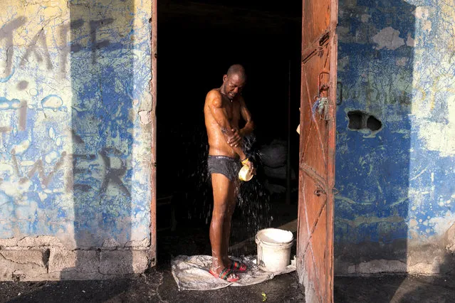 In this December 3, 2019 photo, Odolph Jeudy, a charcoal seller, bathes, framed in the entrance of his shop in the Cite Soleil slum of Port-au-Prince, Haiti. When the new round of protests began in mid-Sept., Haiti's economy was already fragile, but the protests also squeezed incomes, shuttered businesses and disrupted the transportation of basic goods like charcoal, the main source of energy in the country. (Photo by Dieu Nalio Chery/AP Photo)