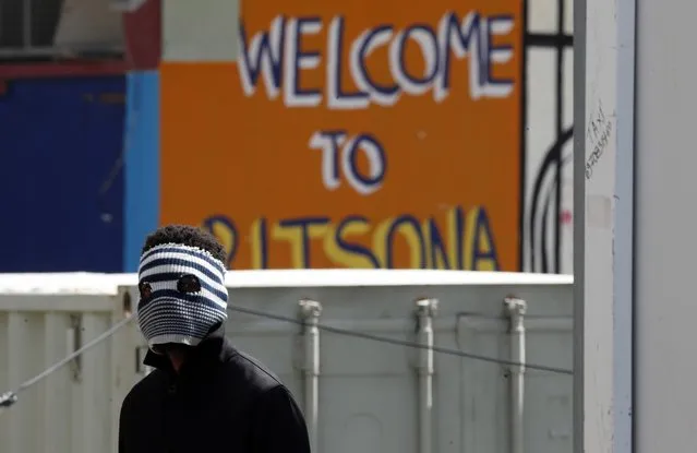 A young migrant covering his face to protect from the new coronavirus stands at the entrance of the Ritsona refugee camp about 80 kilometers (50 miles) north of Athens on Thursday, April 2, 2020. Greek authorities have placed the refugee camp under 14 days quarantine after 20 of its residents tested positive for the COVID-19. During this period nobody would be allowed in or out of the facility. (Photo by Thanassis Stavrakis/AP Photo)