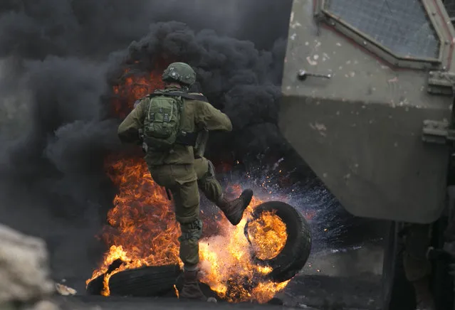 An Israeli soldier removes burning tires from the road during clashes with Palestinian protesters following a demonstration against the expropriation of Palestinian land by Israel in the village of Kfar Qaddum, near Nablus in the occupied West Bank, on September 15, 2017. (Photo by Jaafar Ashtiyeh/AFP Photo)