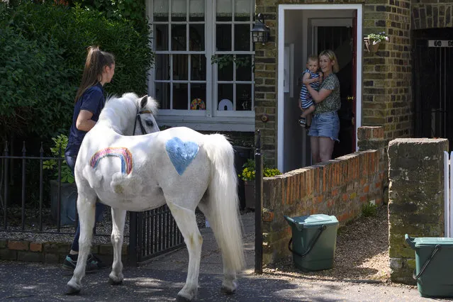 Bryony Blant (R) and daughter Alice (C), who's 2nd birthday it is today, stand on their doorstep looking at Welsh mountain pony Annie's Wizz held by handler Daisy Cinque (L) outside their home in Twickenham, south west London on April 23, 2020. Park Lane Stables are taking the fun to peoples' windows during the novel coronavirus lockdown in an initiative called “Tiny pony at your window”. (Photo by Justin Tallis/AFP Photo)
