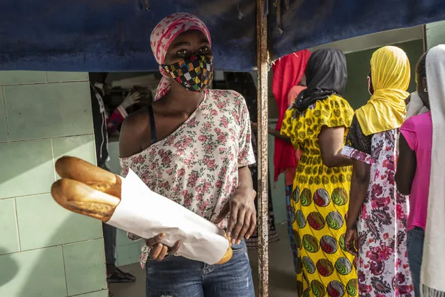 In this photo taken Saturday, April 25, 2020, Ndyeye Fatou, the daughter of Bara Tambedou, wears a patterned face mask as she buys bread for her family on the first day of the Muslim holy month of Ramadan, in Dakar, Senegal. This year the family is celebrating Ramadan at home, with prohibitions on public gatherings and a dusk-to-dawn curfew in place to curb the spread of the new coronavirus. (Photo by Sylvain Cherkaoui/AP Photo)