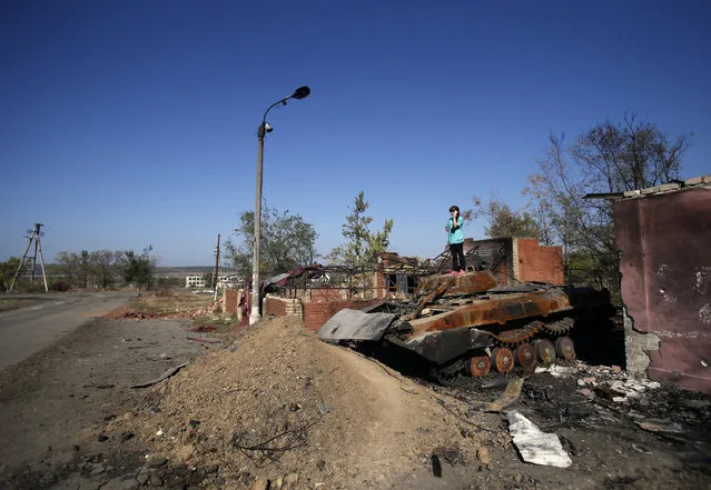 A girl stands on the remains of a charred tank to get better reception on her mobile phone in the village of Novosvitlivka, eastern Ukraine, Monday, September 15, 2014. The village was severely damaged during fighting between government troops and the separatist rebels that eventually took control there in late August. (Photo by Darko Vojinovic/AP Photo)