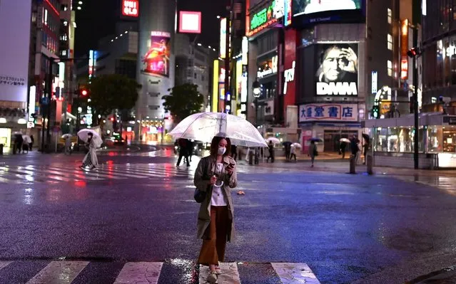 A woman wearing a face mask amid concerns of the COVID-19 coronavirus, uses an umbrella to shelter from the rain while crossing a street in Tokyo on May 19, 2020. (Photo by Charly Triballeau/AFP Photo)