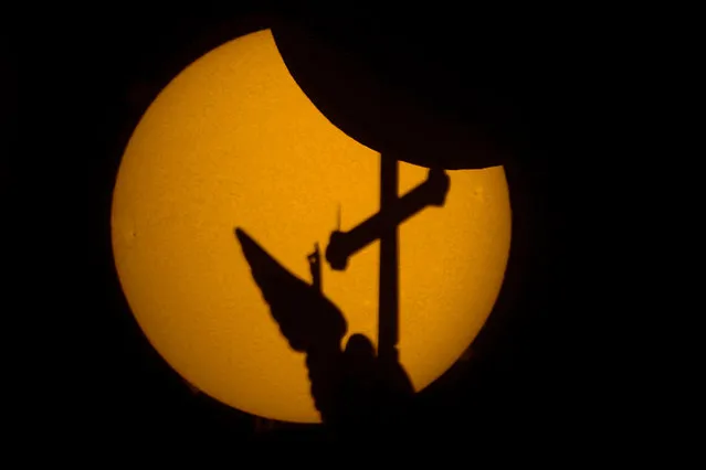 The city landmark, a weather vane in the form of an angel fixed atop a spire of the Saints Peter and Paul Cathedral, is silhouetted against the sun during a partial solar eclipse in St. Petersburg, Russia, Tuesday, October 25, 2022. The photo was taken through a telescope with a hydrogen-alpha (H-alpha) narrow spectrum filter that permits examination of the sun's surface activity. (Photo by Dmitri Lovetsky/AP Photo)